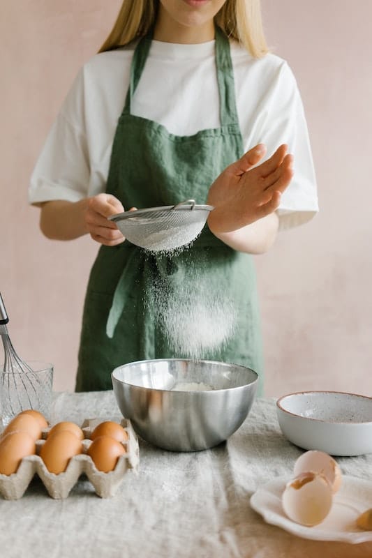 žena peče a prosévá si mouku do mísy