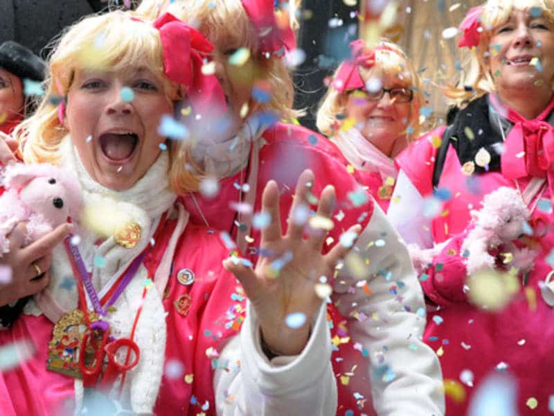 Rozjívené ženy v růžovém s nůžkami na krku se chystají na muže a chtějí jim stříhat kravaty, zvyk zvaný Weiberfastnacht.