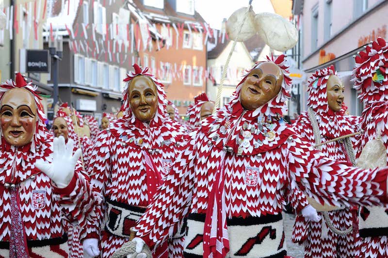 Krásné dřevěné propracované masky kráčejí průvodem ve švábsku-alemansku, mají červenobílé kostýmy.